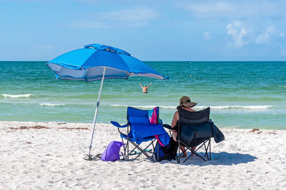 Beach chairs under a blue umbrella on a quiet white-sand Gulf beach